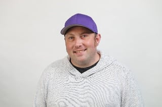 Alex Hillman headshot. He is a white male wearing a purple baseball cap and white hoodie.