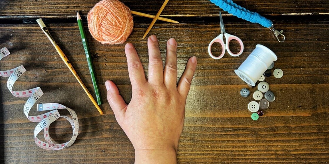 A photo of hands with pencils, yarn, thread, and various crafting items.