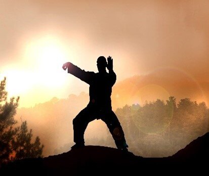 Silhouette of a male figure practicing qigong with foggy and misty mountaintops behind him.